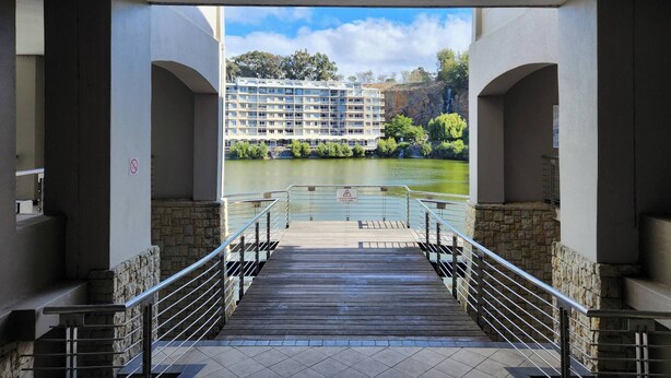 Vue depuis une galerie couverte sur un plan d’eau, avec un hôtel en arrière-plan.