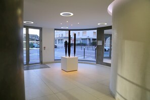 A modern lobby with glass doors, a central white pedestal, and recessed ceiling lighting. - Sunny terrace near the Canal de l'Ourcq - quiet & bright (Paris)