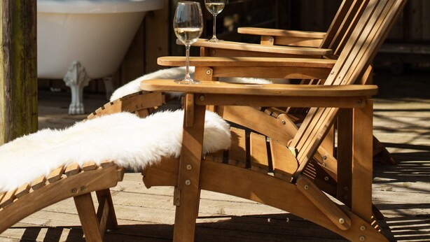 Una terraza de madera con una silla de descanso, una copa de vino y una bañera.
