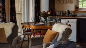 Un comedor con una mesa dispuesta para cuatro personas, un refrigerador, una tetera y un ventanal con cortinas.
