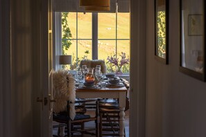 A dining area with a table set for four, a fur throw, and a view of a grassy field through large windows.