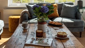Una sala de estar acogedora con una mesa de centro de madera, un sofá y vistas a colinas ondulantes a través de amplios ventanales.