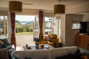A living room with a sofa, a coffee table, a TV, and a view of a garden.