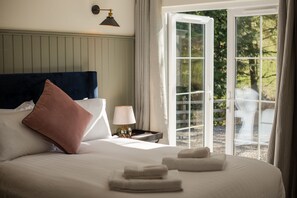 A hotel room with a bed, pillows, a nightstand with a lamp, and a view of the outdoors through a glass door. - Charming one bed cottage (Oban)
