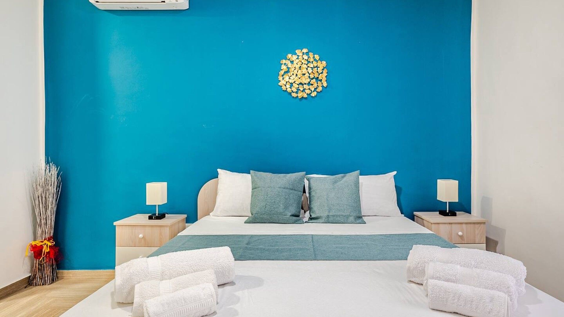 A hotel room with a bed, two bedside tables, a lamp on each table, a blue wall, and a decorative wall piece.