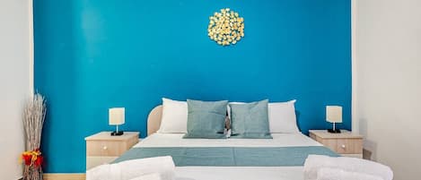 Een hotelkamer met een bed, twee nachtkastjes, een lamp op elk kastje, een blauwe muur en een decoratief object aan de muur.