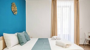 Una camera d'albergo con un letto, cuscini, una coperta, una sedia e una finestra con tende.