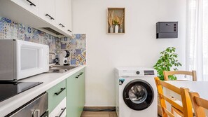 Cocina compacta con microondas, tostadora y lavadora, un salpicadero con diseño y una pequeña planta.