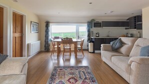 A spacious living area with a dining table, sofa, and kitchen in the background. - Courtyard Farm Cottages (Boscastle)