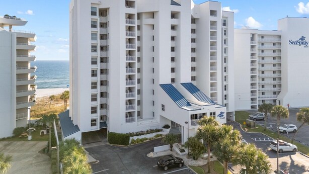 Un hotel de varios pisos con balcones, un estacionamiento y vista al océano.