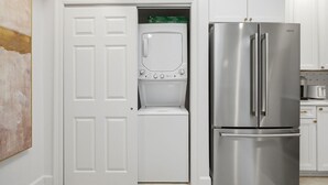 Cocina compacta con refrigerador de acero inoxidable, lavadora y secadora integradas, y armarios blancos.
