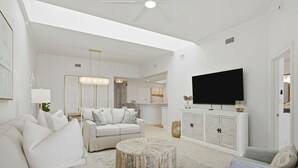 Amplia sala de estar con un sofá blanco, una mesa redonda para café y un televisor montado en un mueble blanco.