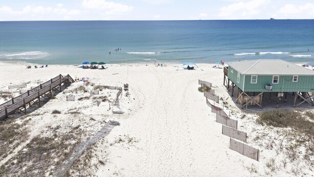 A beach with a wooden boardwalk, a lifeguard tower, and a sandy beach area. - Rookery III 6005 - Peach and Quiet (Gulf Shores)