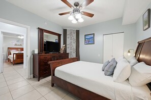 Quarto com cama, penteadeira, televisão, ventoinha de teto e porta.