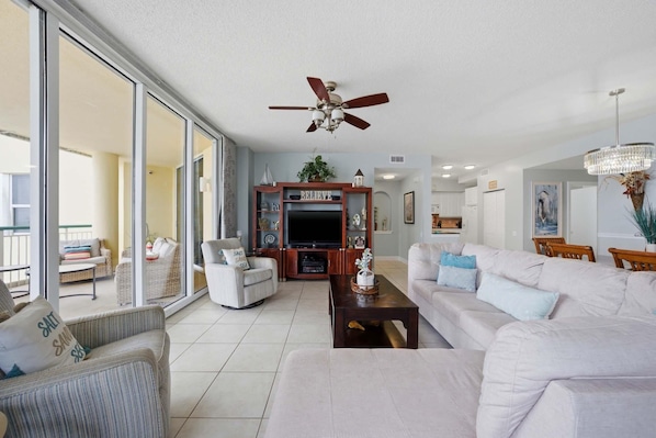 A spacious living room with a large TV, comfortable seating, and a ceiling fan. - Beach Colony East 7B (Pensacola)