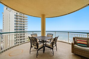 Varanda com mesa e cadeiras, um sofá e vista para o mar e edifícios.