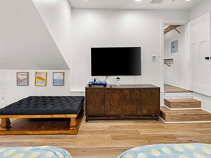 A modern bedroom with a large bed, a wooden dresser, a flat-screen TV, and a staircase leading to an upper level. - 5BR Mountain Retreat | Indoor Spa + Sauna + Views (Clyde)