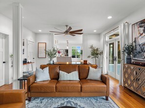 A modern living room with a brown leather sofa, a dining area, and a kitchen in the background. - 5BR Mountain Retreat | Indoor Spa + Sauna + Views (Clyde)