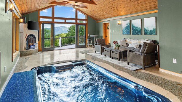Ruime binnenruimte met een jacuzzi, houten balkenplafond, een open haard en uitzicht op het omliggende landschap.