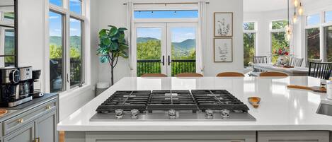 Une cuisine moderne dotée d’un îlot central, de grandes fenêtres et offrant une vue sur la verdure.