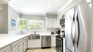 A modern kitchen with white cabinetry, stainless steel appliances, and a window with blinds. - Family Beach Retreat Near Coligny Beach (Hilton Head Island)