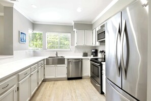 A modern kitchen with white cabinetry, stainless steel appliances, and a window with blinds. - Family Beach Retreat Near Coligny Beach (Hilton Head Island)
