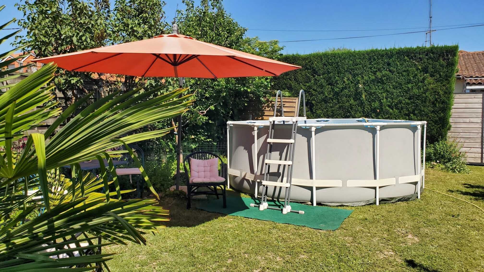 A backyard with a small playhouse, a red umbrella, and a chair.. The little house