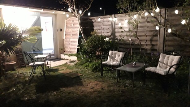 Eine Terrassenanlage mit Tisch und zwei Stühlen, einer Ziegelwand und Lichterketten.