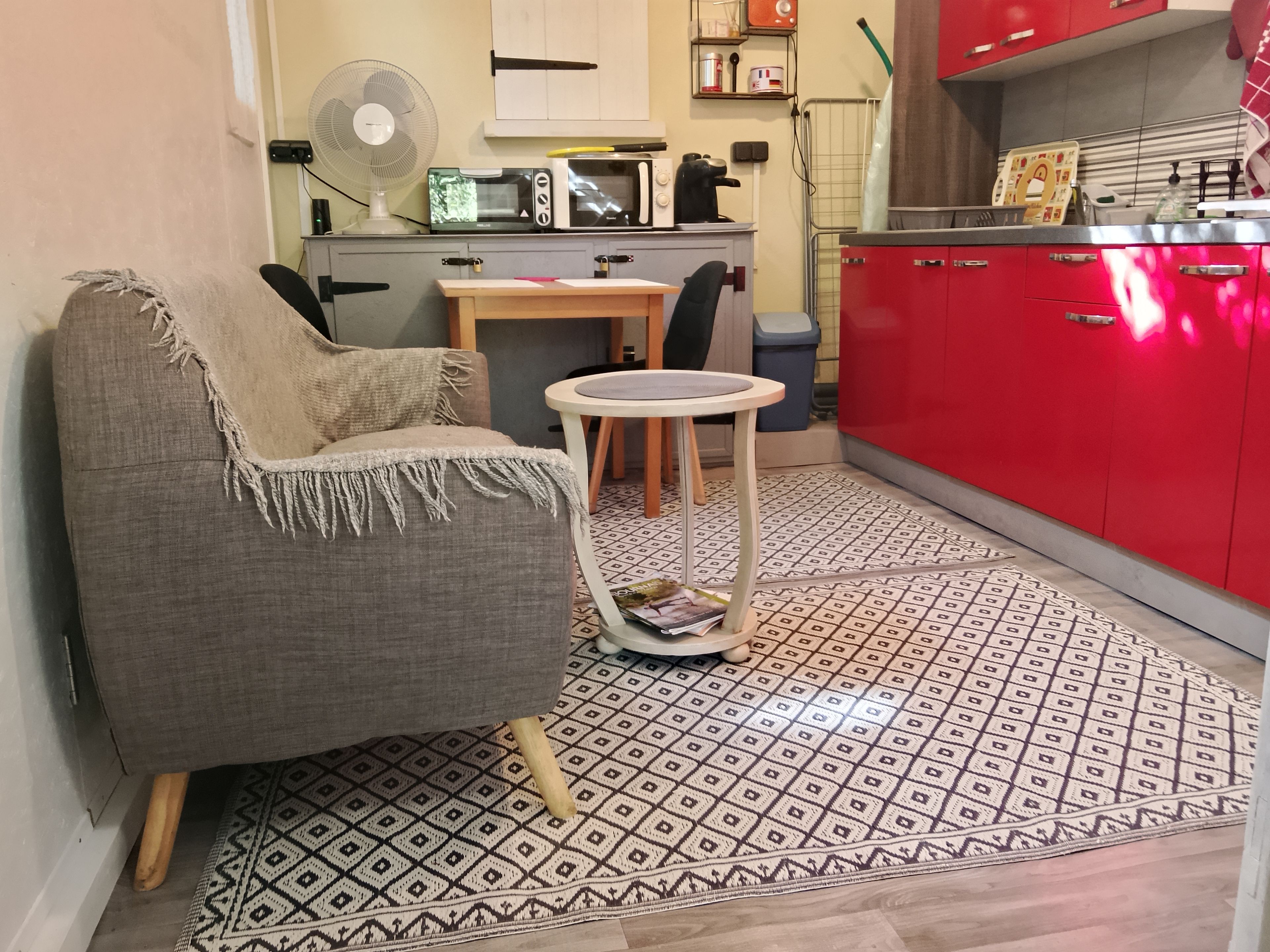Un espai vital compacte amb un sofà, una taula rodona petita, una zona de cuina amb armaris vermells i un paviment amb disseny.