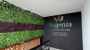 Un escalier avec une rampe noire, un mur orné d’un motif de feuilles vertes et une enseigne indiquant « Fugenia Garden Suites ».