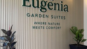 Un mur d’entrée orné du nom « Eugenia Garden Suites » et d’un slogan : « L’endroit où la nature rencontre le confort ». De part et d’autre du mur, on trouve deux plantes en pot.