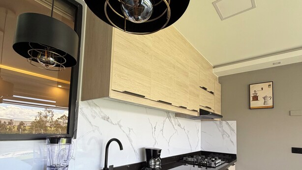 Une cuisine moderne avec un plan de travail noir, une cuisinière encastrée, un mixeur et un luminaire suspendu.