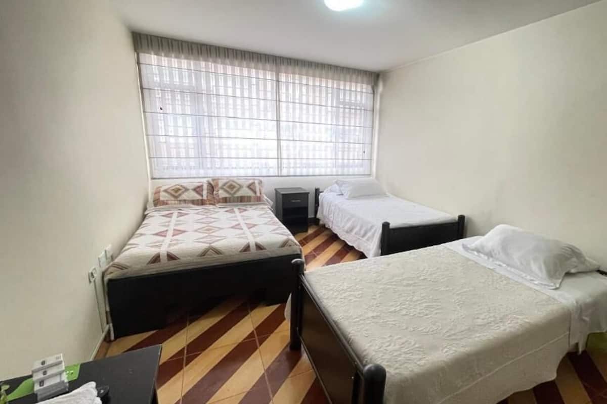 Una habitación con dos camas individuales, una ventana con persianas, una mesita y una silla.