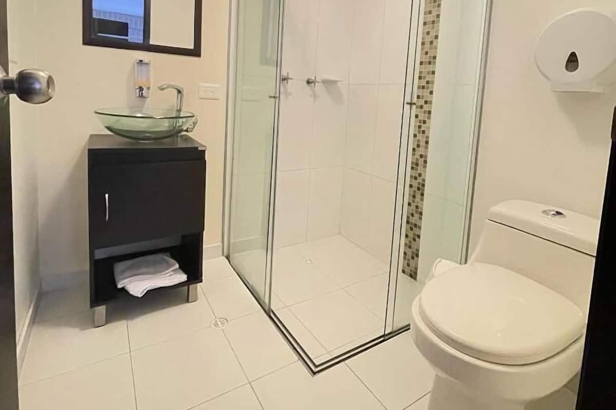 Un baño con ducha de vidrio, lavamanos de cristal, inodoro y espejo.