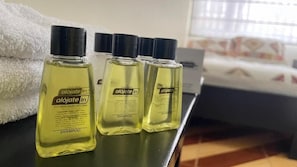 Three bottles of shampoo on a counter with a towel and a bed in the background. - Hotel Alojate In (Bogotá)