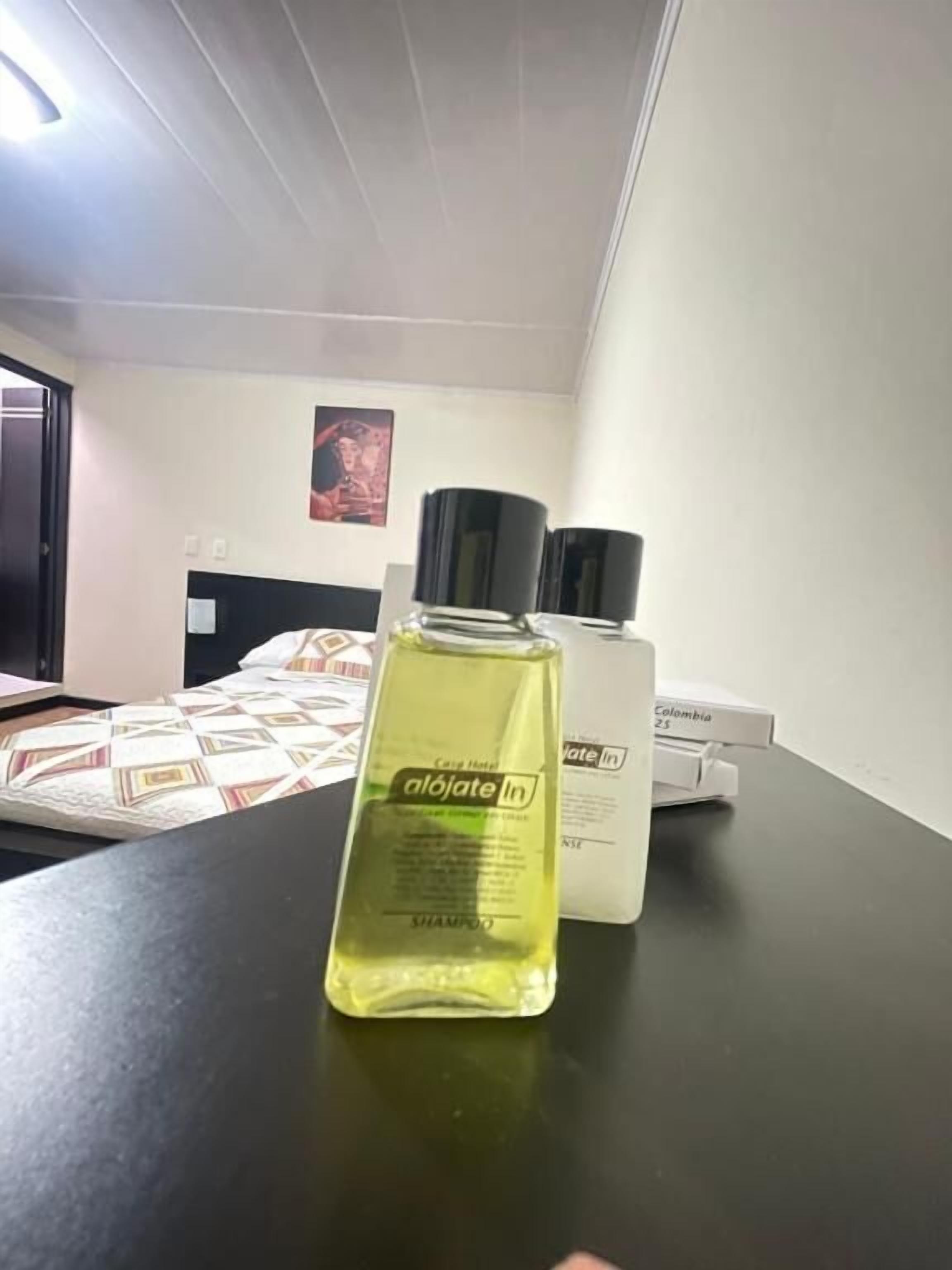 A hotel room with a bed, a table, and a bottle of shampoo.