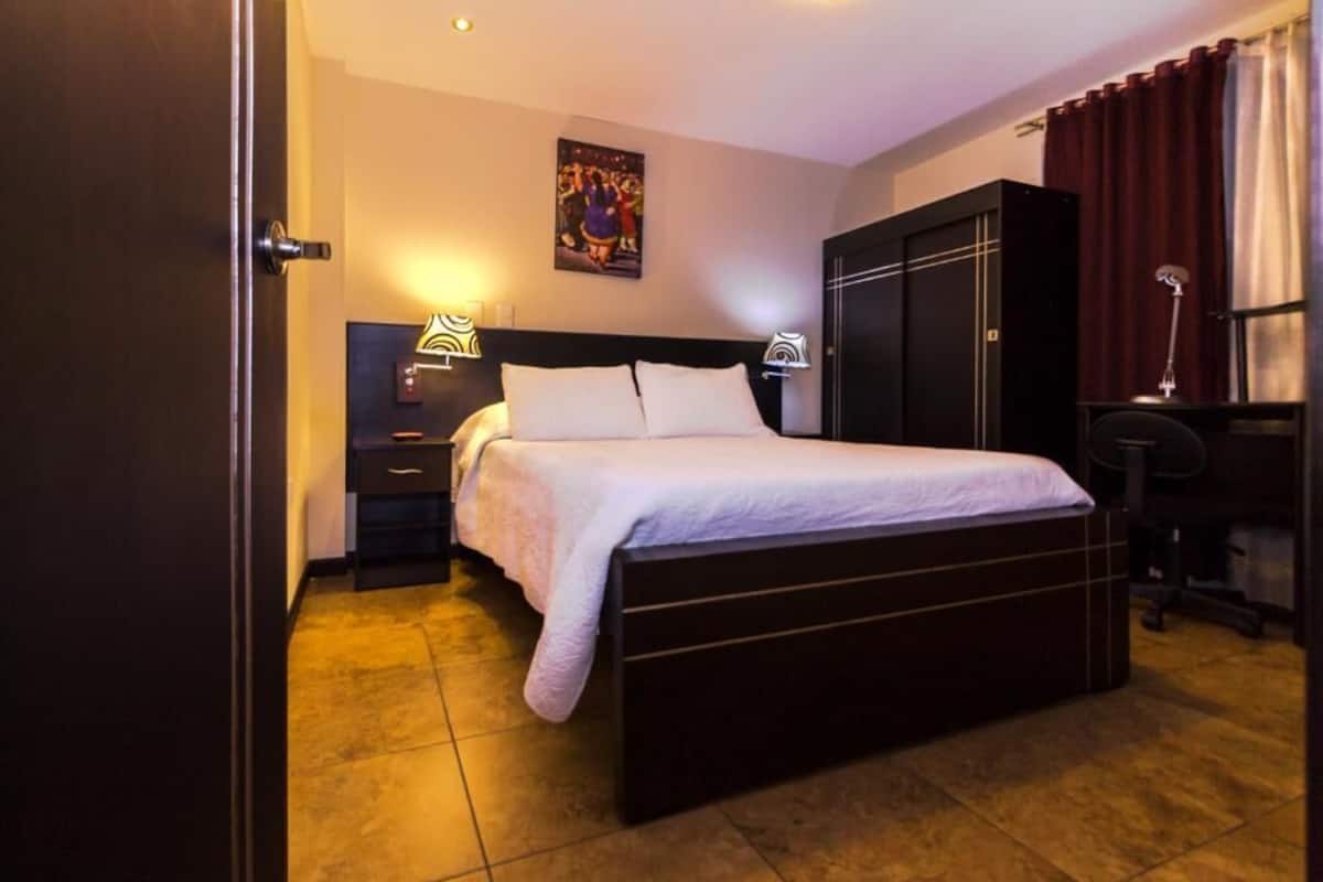 Una habitación de hotel con cama, mesitas de noche, escritorio y armario.