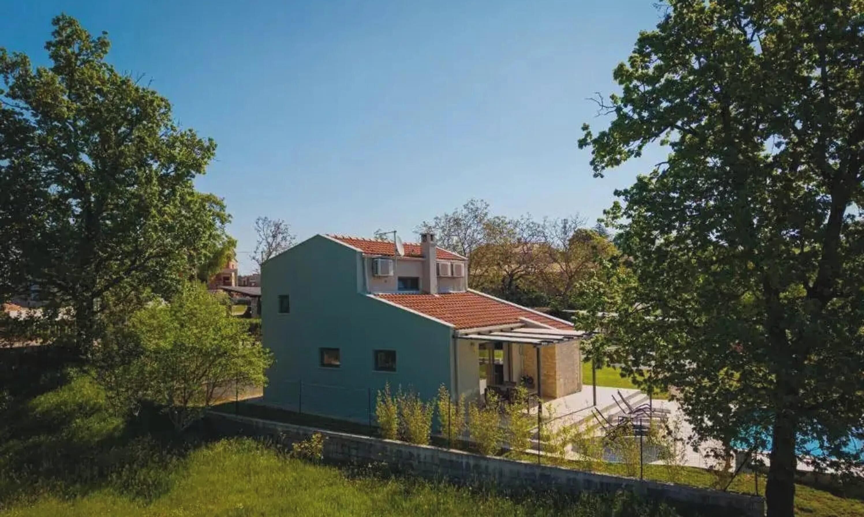 Una casa moderna de dos pisos con techo de tejas rojas, rodeada de vegetación y árboles.