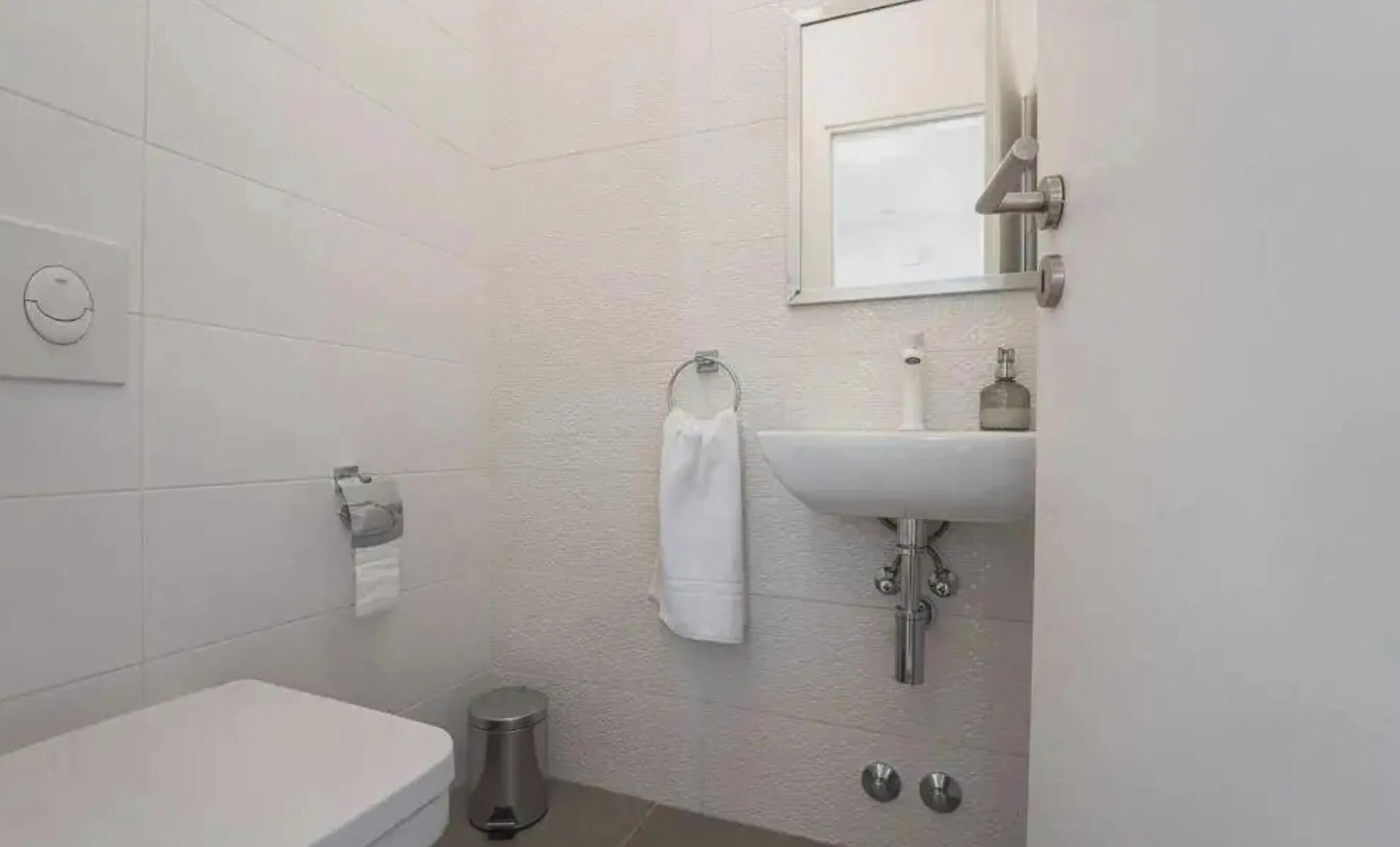 Un baño con inodoro, lavamanos y un cubo de basura.