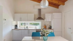 Una cocina moderna con armarios blancos, una isla central y vista a la calle por la ventana.