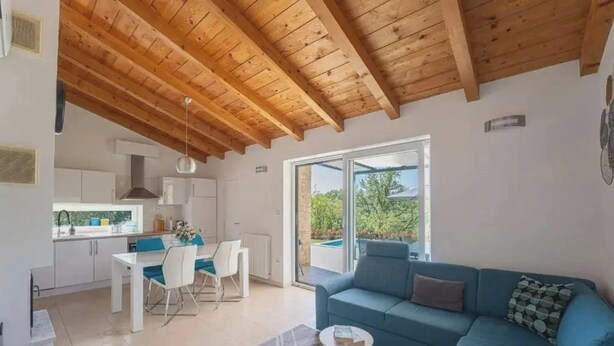 Un interior moderno con techo de madera, zona de comedor, sofá azul y vistas a través de un ventanal.