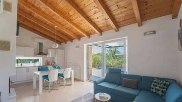 A modern interior with a wooden ceiling, a dining area, a blue sofa, and a view through a glass door.