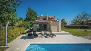 Una casa de dos pisos con piscina, mobiliario exterior y jardín.