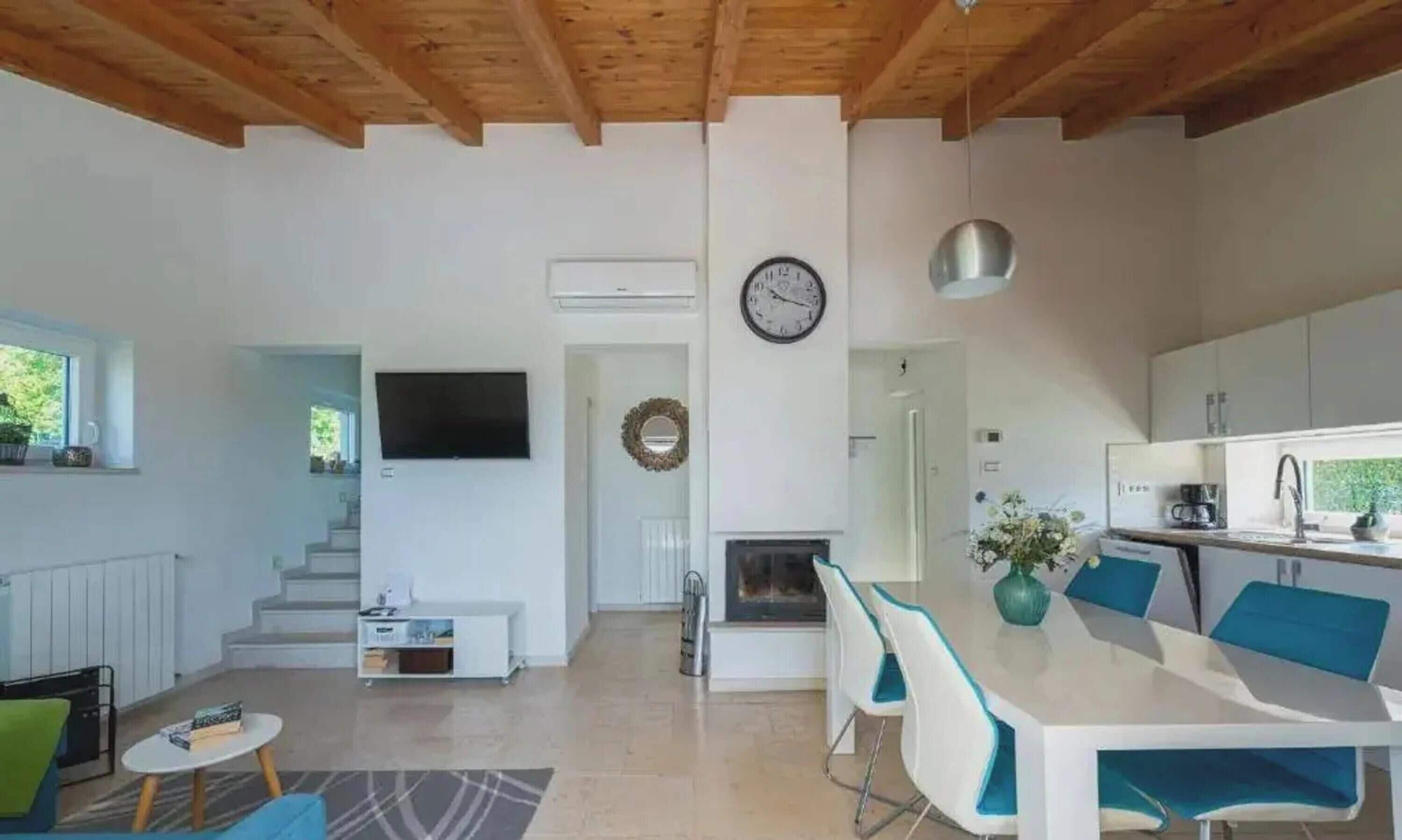 A modern interior with a dining area, kitchen, and living space, featuring a TV, clock, and staircase.