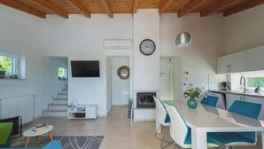 Un interior moderno con comedor, cocina y sala de estar, destacando un televisor, un reloj y una escalera.