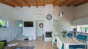 A modern interior with a dining area, kitchen, and living space, featuring a TV, clock, and staircase.