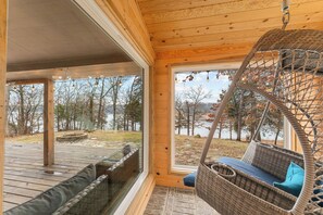 A wooden interior with a wicker swing chair and a view of a lake. - Quiet Modern Lakefront House with Amazing Views (Golden)