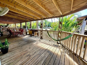A wooden deck with a hammock, chairs, and potted plants.