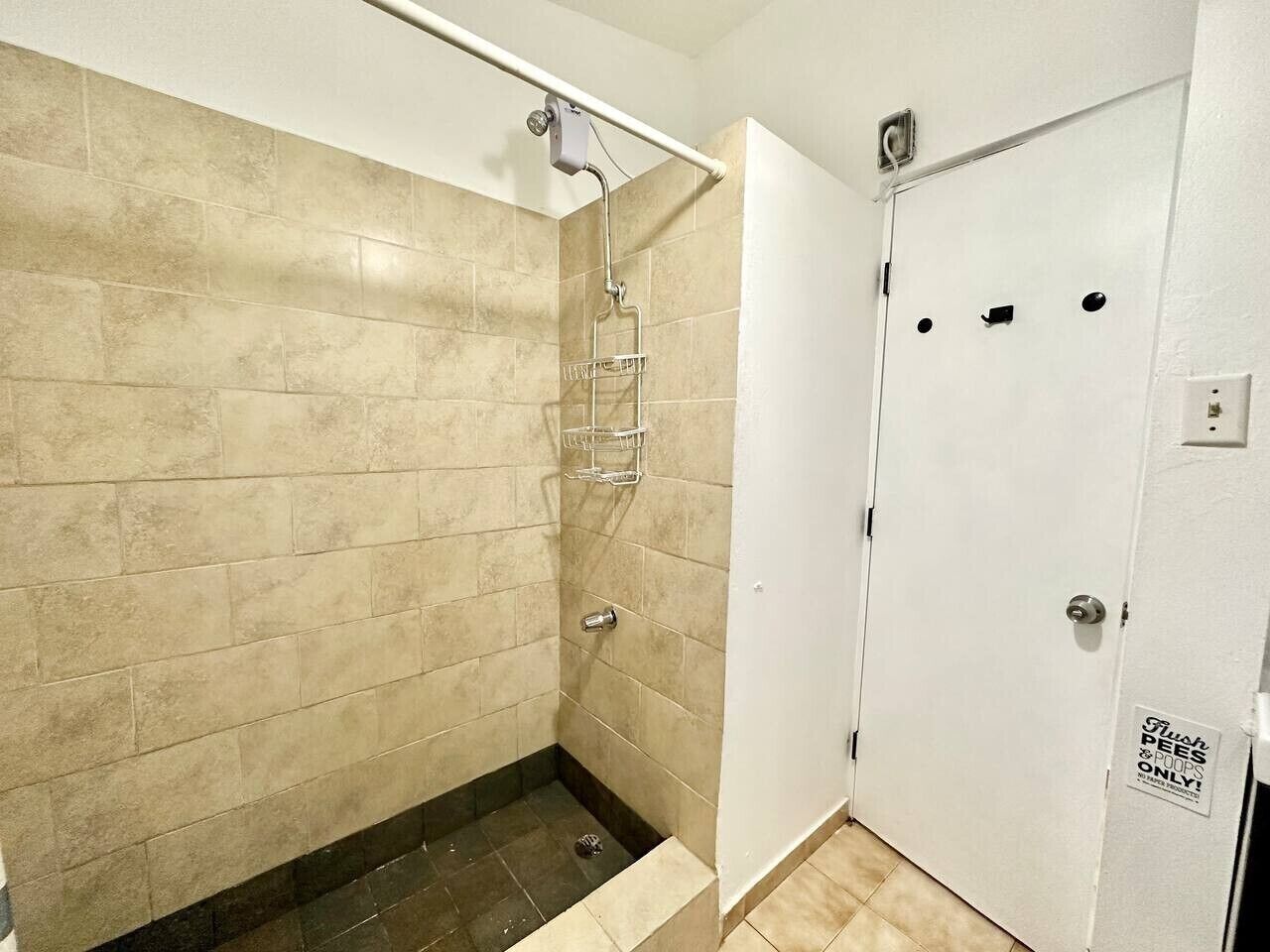 A bathroom with beige tiles, a shower, a toilet, and a door with a sign indicating it's for 'Flush Peees & Poops Only.'