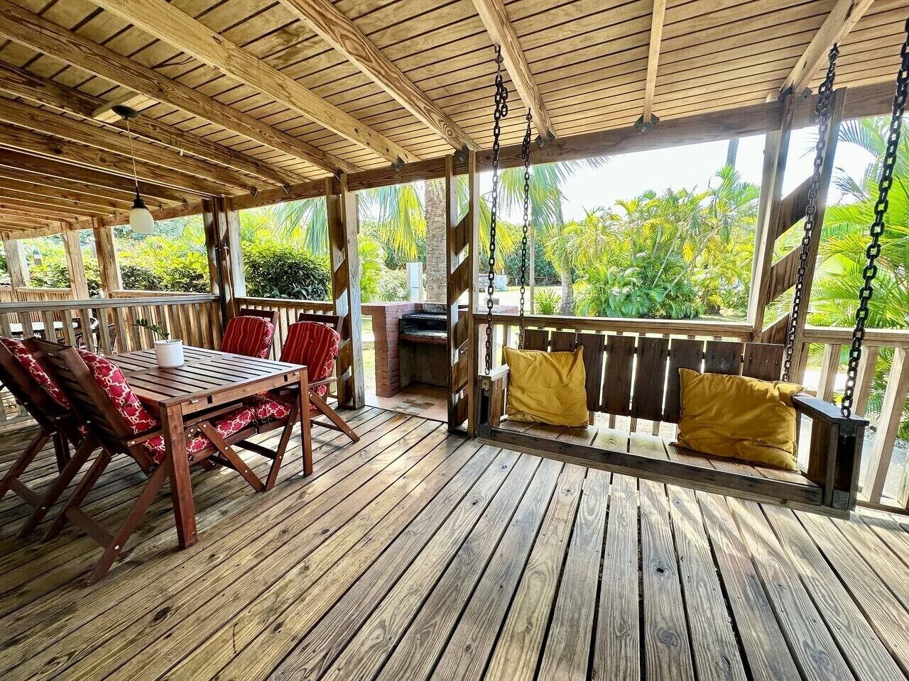 Eine Holzterrasse mit Tisch, Stühlen, einer Schaukel und einem Grillbereich.